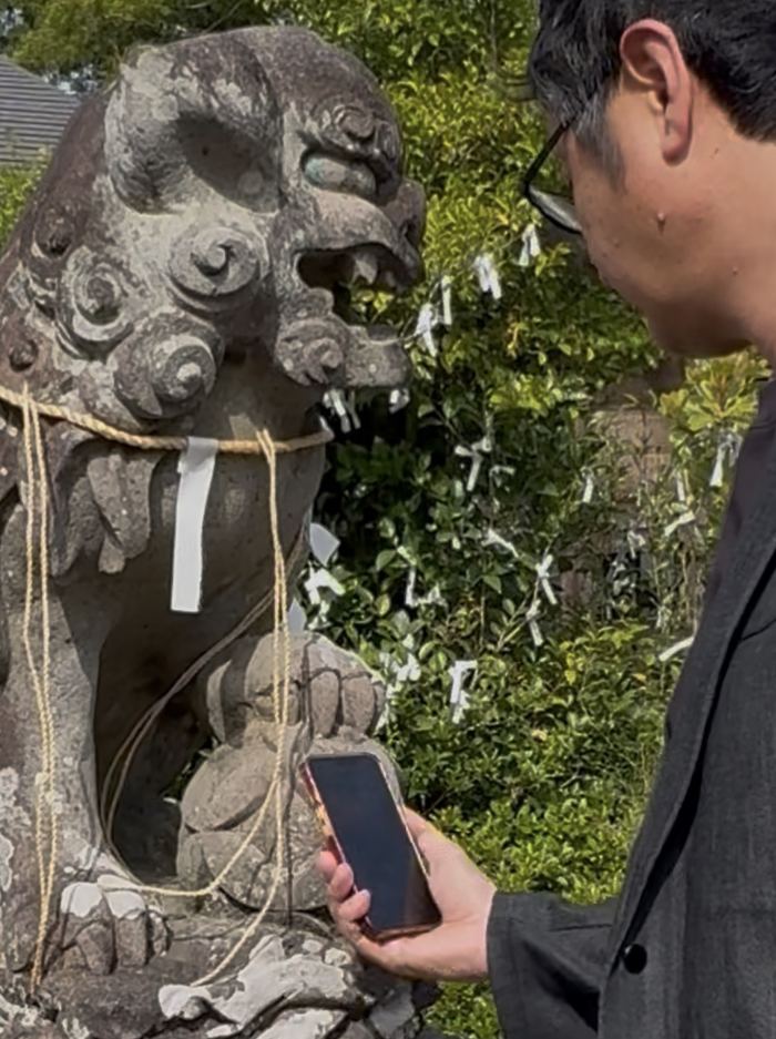荒雄神社の狛犬の前でスマートフォンをかざす様子